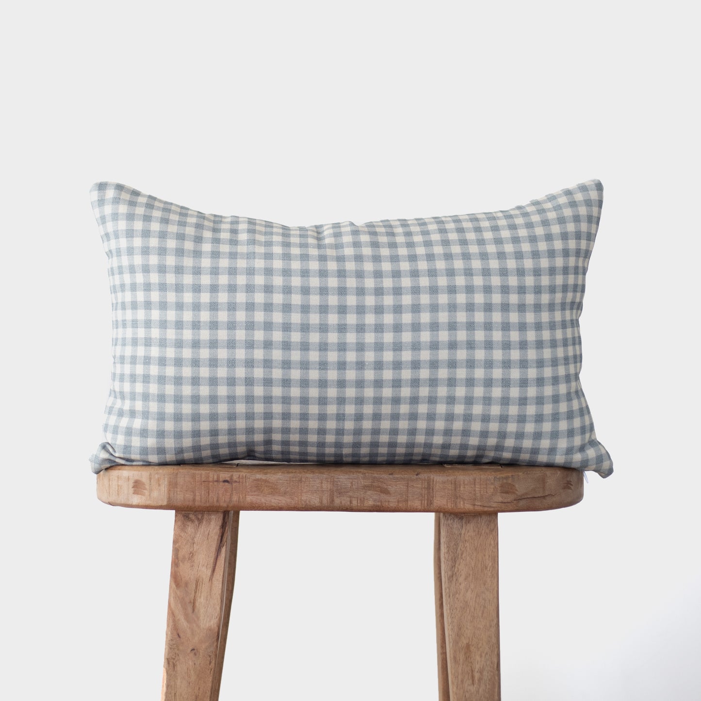 Dusty blue and white gingham patterned pillow cover resting on wooden bench.