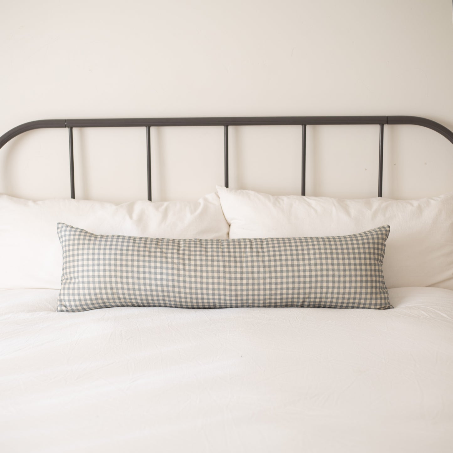 Dusty blue and white gingham check lumbar pillow on bed with white bedding and metal headboard.