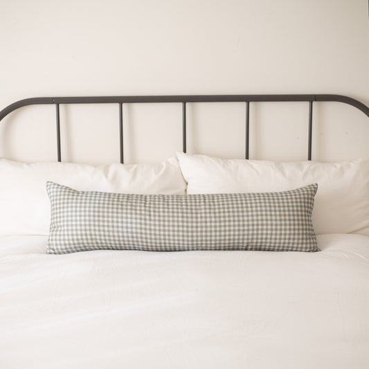 Dusty blue and white gingham check lumbar pillow on bed with white bedding and metal headboard.
