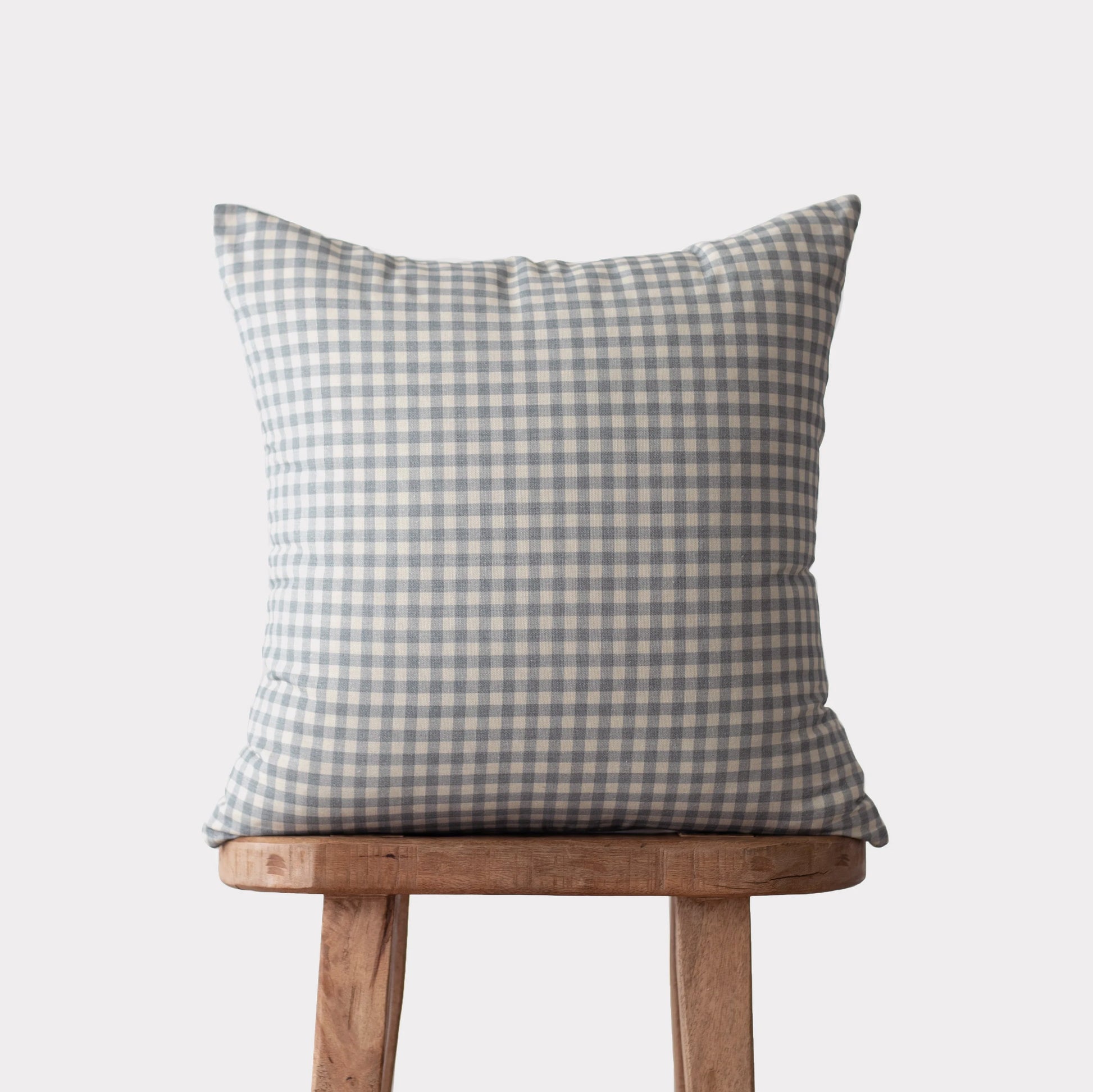 Dusty blue and white gingham checkered pillow on wooden stool.