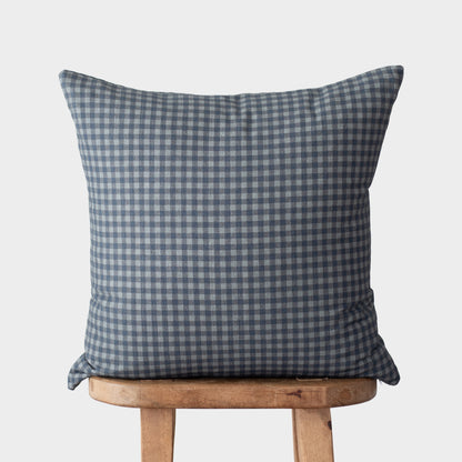 Navy and white gingham patterned square pillow displayed on a wooden stool.