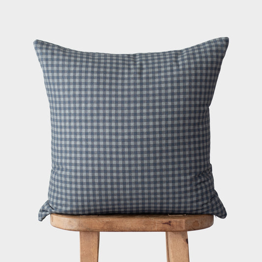 Navy and white gingham patterned square pillow displayed on a wooden stool.