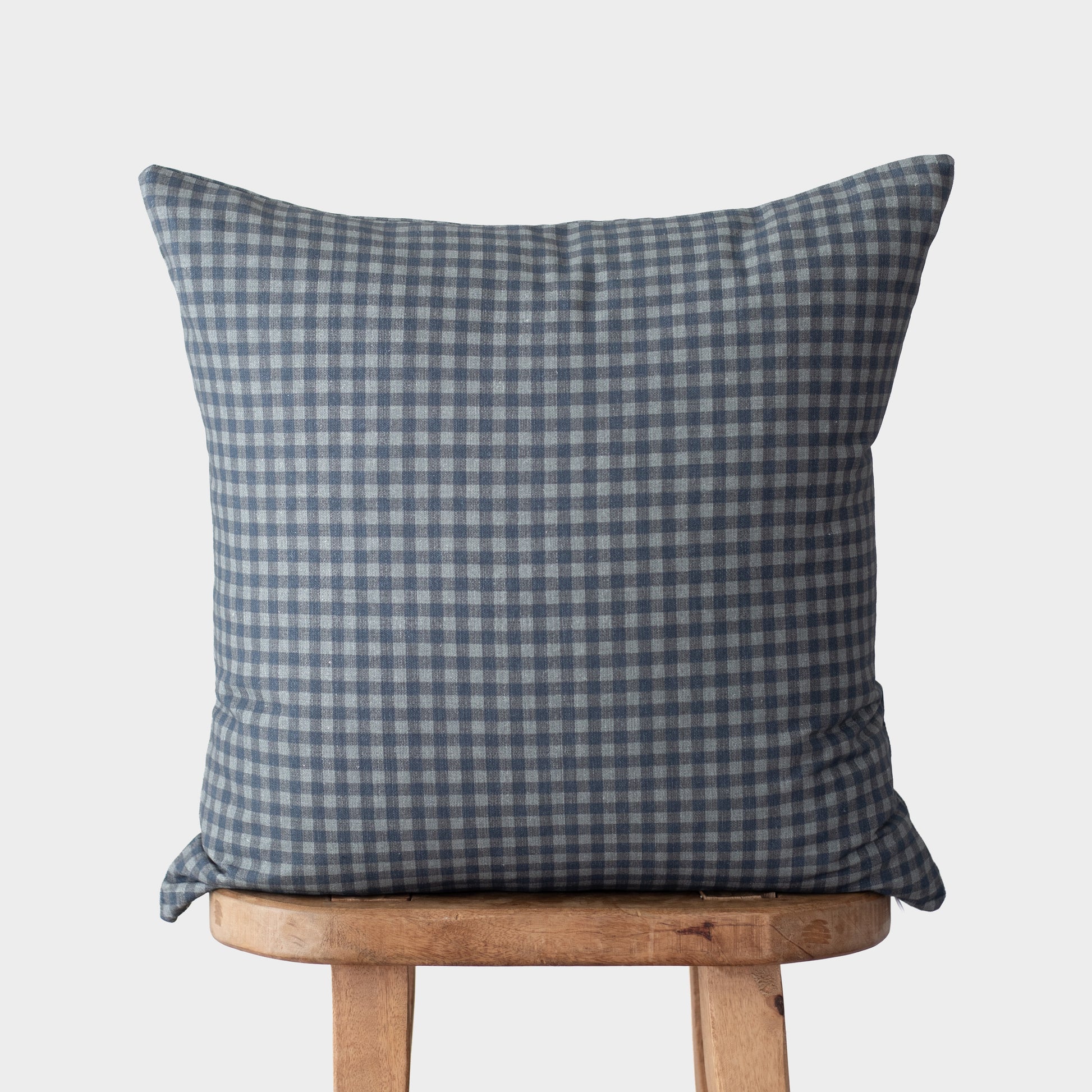 Blue and white gingham pillow cover on wooden chair against neutral background.