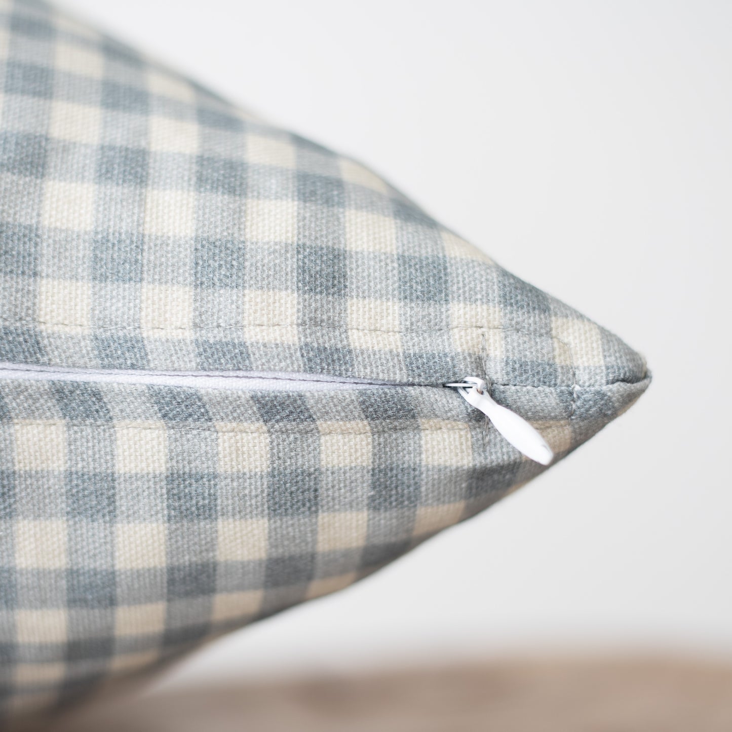 Dusty blue and cream gingham patterned pillow with zipper closure detail visible on seam.