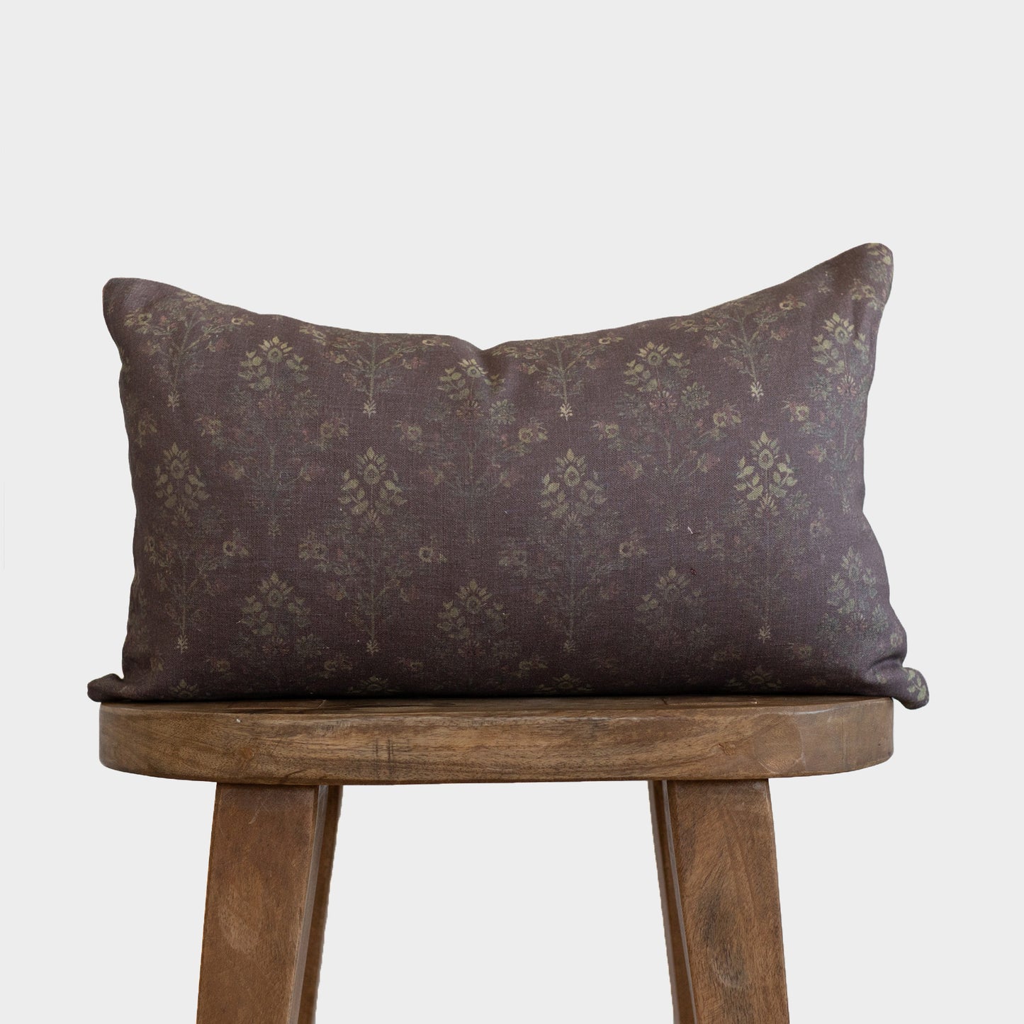 Dark brown linen pillow with damask pattern in muted gold tones, displayed on wooden stool.