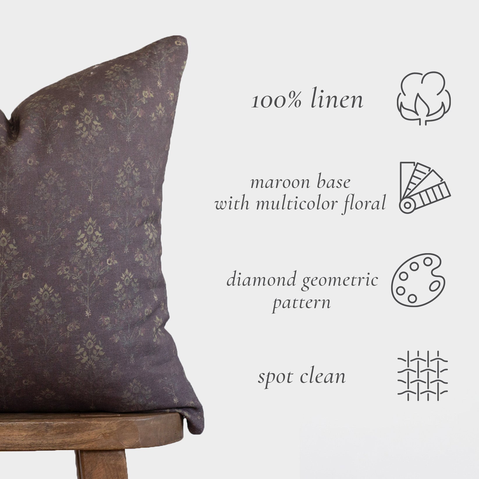 Maroon linen pillow with multicolor floral and diamond geometric pattern, shown on wooden chair.