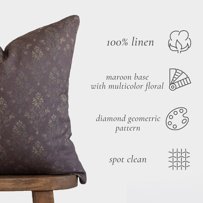 Maroon linen pillow with multicolor floral and diamond geometric pattern, shown on wooden chair.