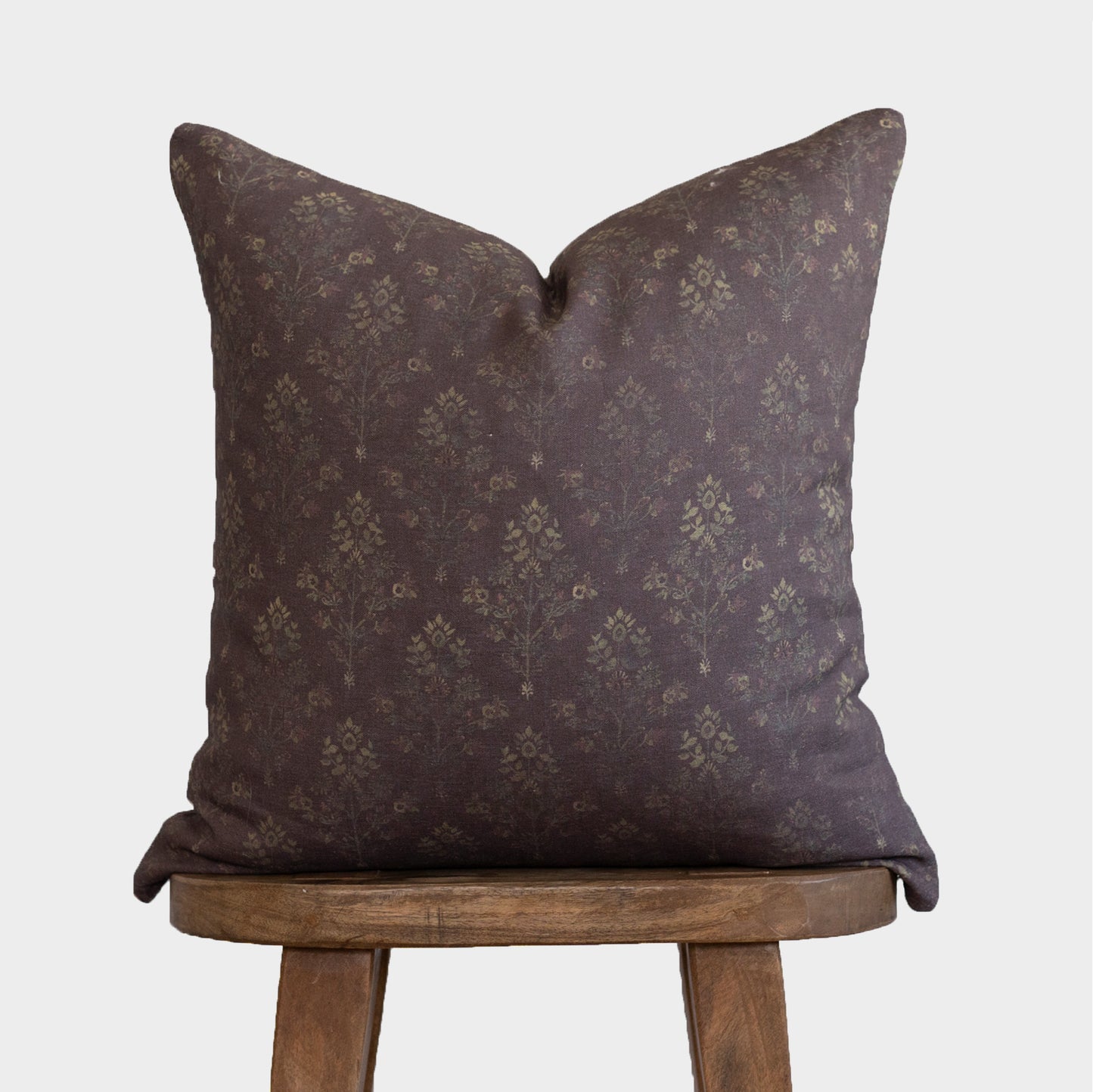 Burgundy linen pillow with damask pattern in muted gold tones, displayed on a wooden stool.