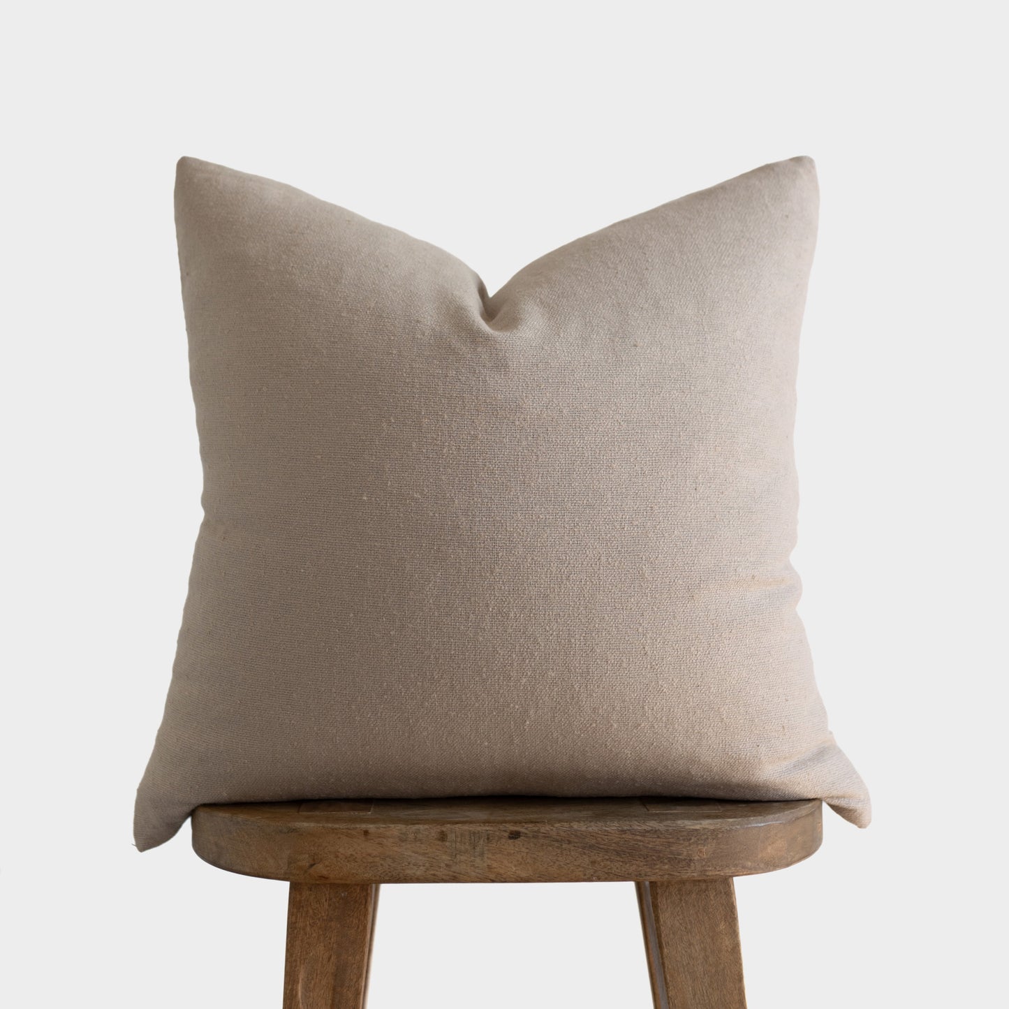 Tan boucle textured pillow with envelope closure displayed on wooden stool.