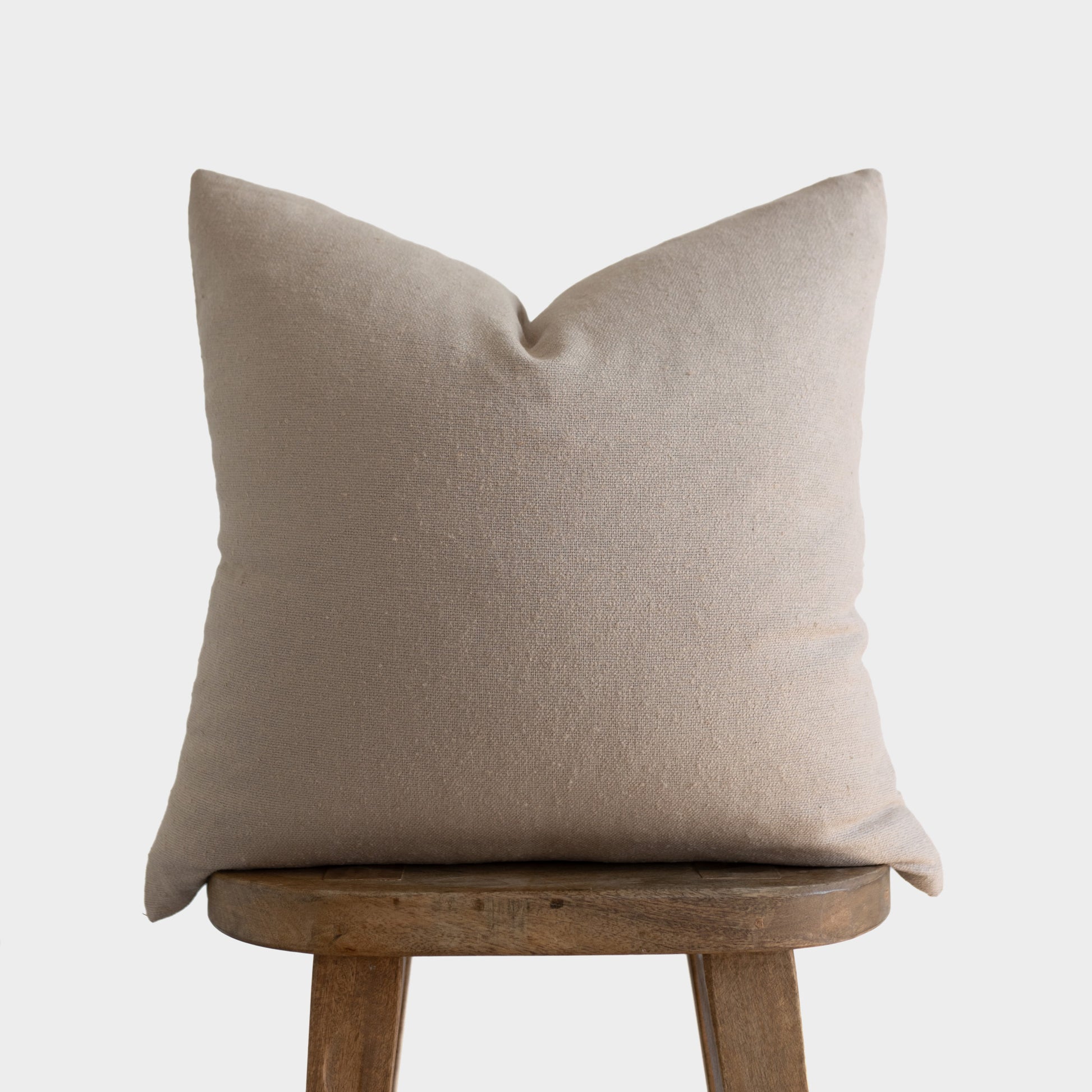 Tan boucle textured pillow with envelope closure displayed on wooden stool.
