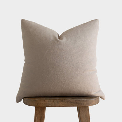 Tan boucle textured pillow with envelope closure displayed on wooden stool.