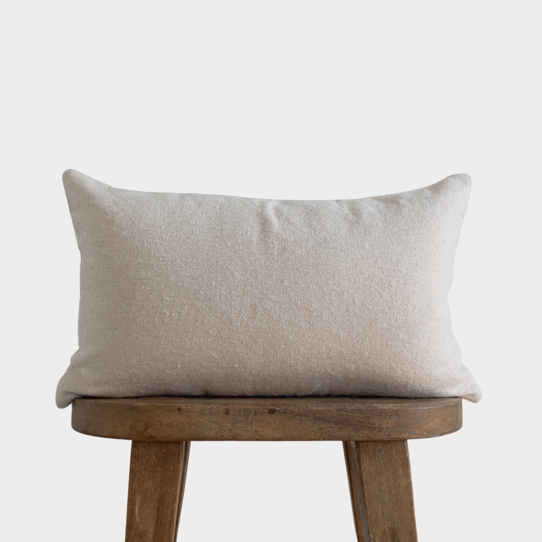 Off-white boucle lumbar pillow with textured fabric displayed on a wooden stool.