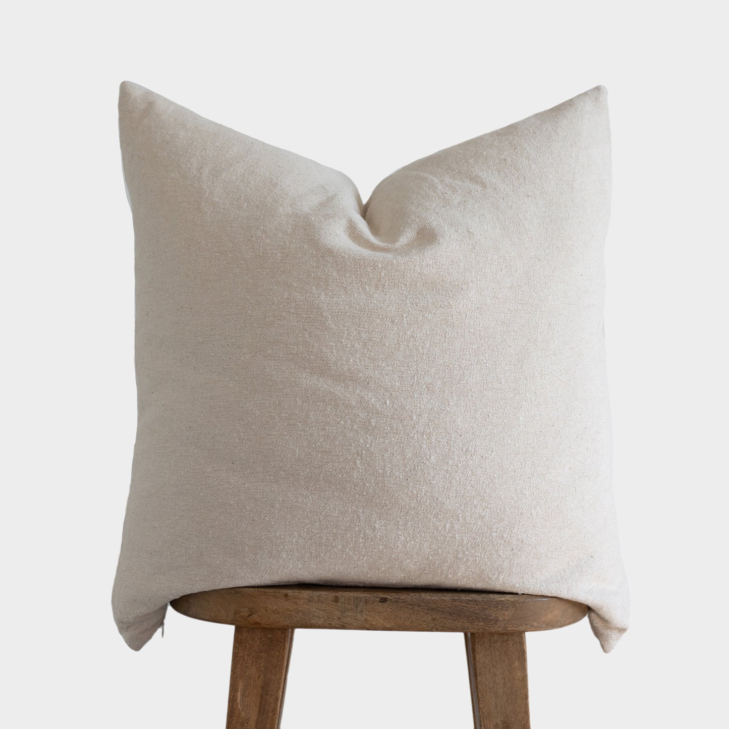 Off-white boucle pillow cover with textured weave displayed on wooden stool.
