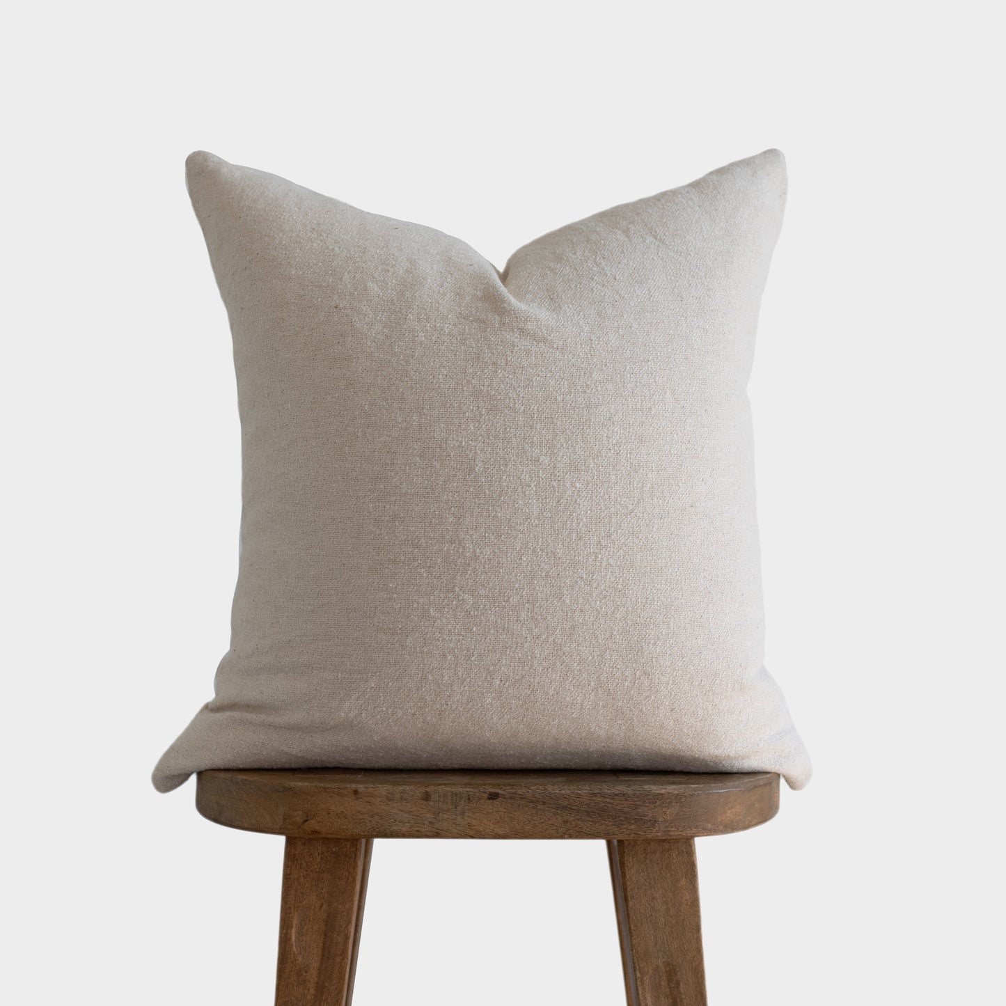 Off-white boucle pillow cover with pointed corners displayed on a wooden stool.