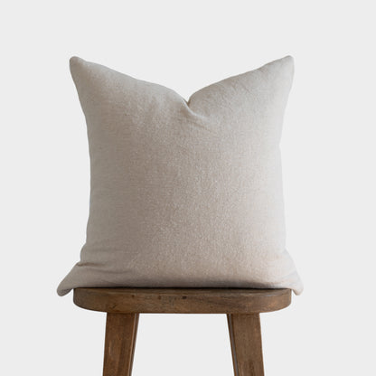 Off-white boucle pillow cover with pointed corners displayed on a wooden stool.