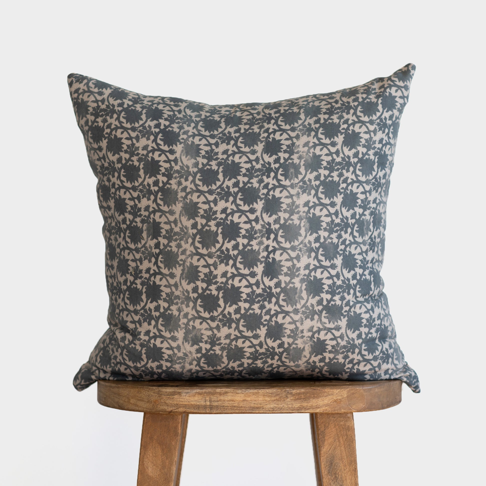 Dark blue and cream damask patterned pillow displayed on wooden stool.