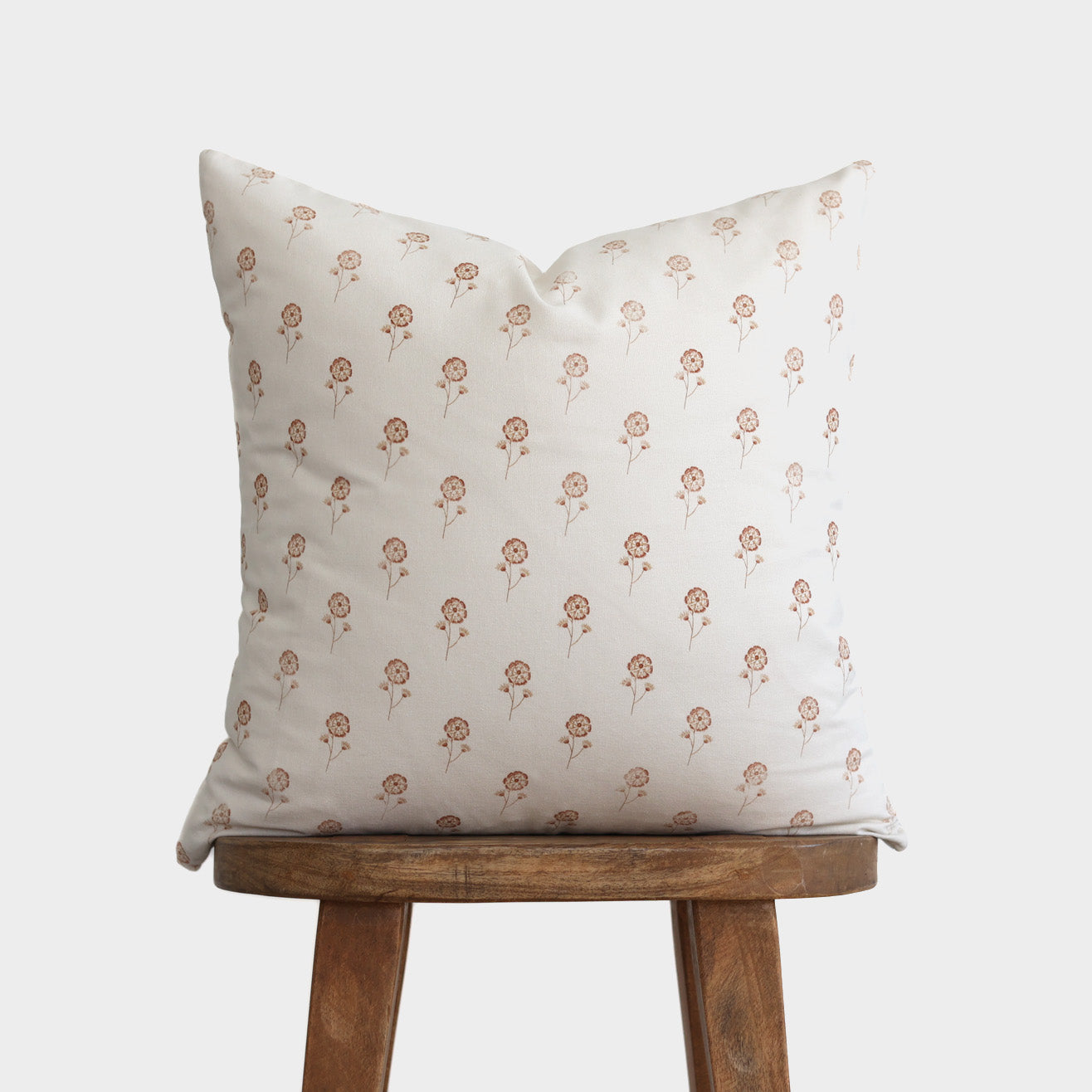 Cream pillow with small buttercup flower pattern in tan, displayed on wooden stool.