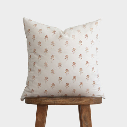 Cream pillow with small buttercup flower pattern in tan, displayed on wooden stool.