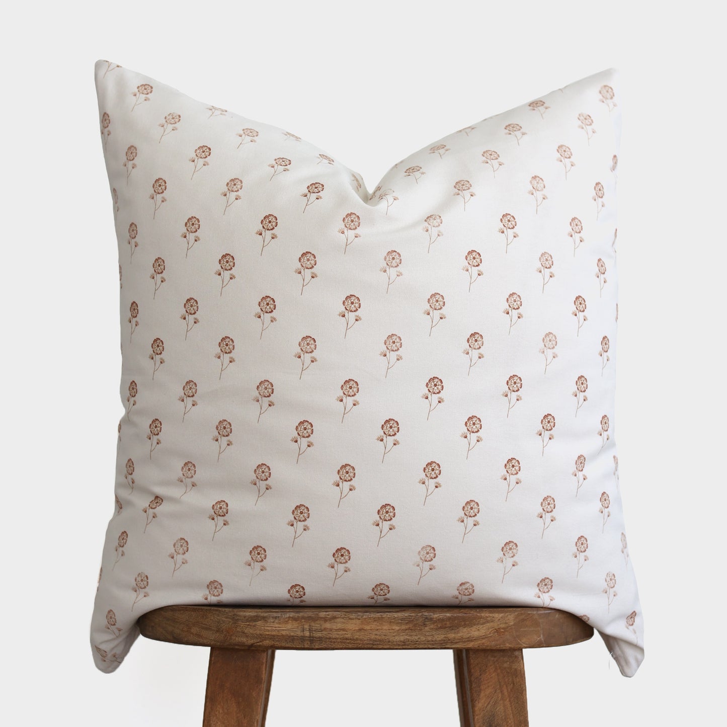 Cream pillow with repeating tan floral pattern resting on wooden stool.