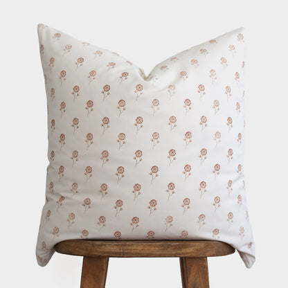 Cream pillow with repeating tan floral pattern resting on wooden stool.