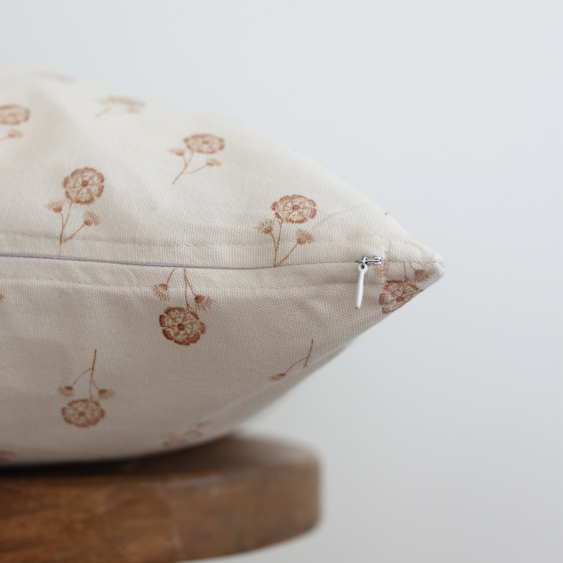 Cream pillow with tan dandelion print and zipper detail, displayed at an angle.