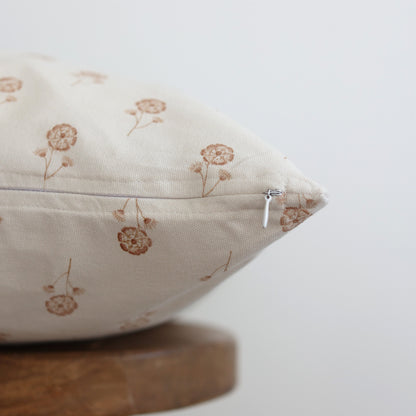 Cream pillow with tan dandelion print and zipper detail, displayed at an angle.