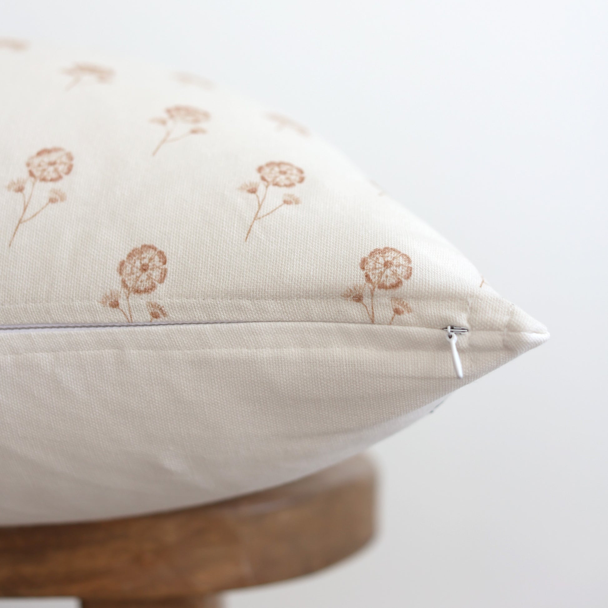 Cream linen pillow with tan embroidered wildflower design and zipper closure on wooden base.