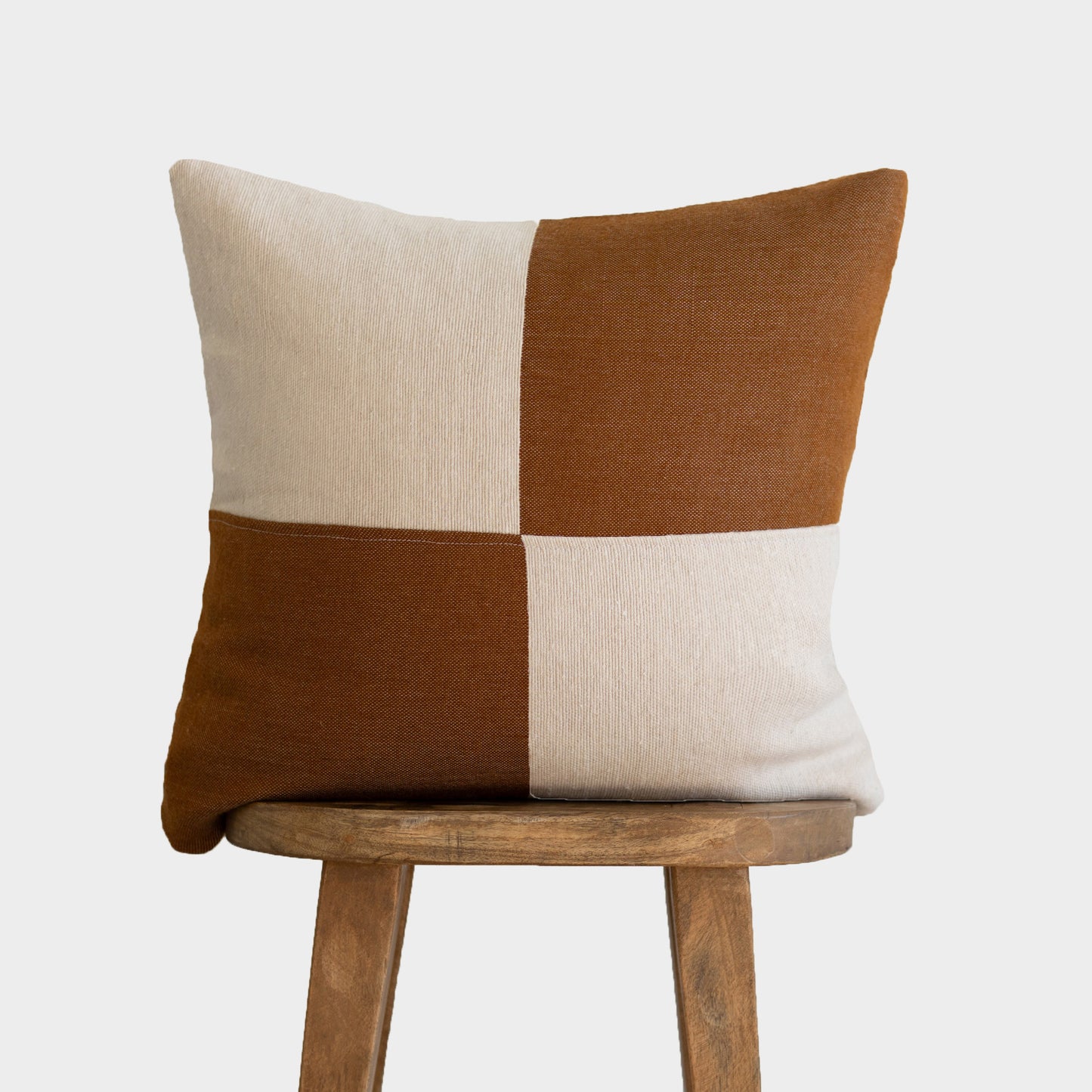 Brown and cream checkered pillow cover displayed on wooden chair back.