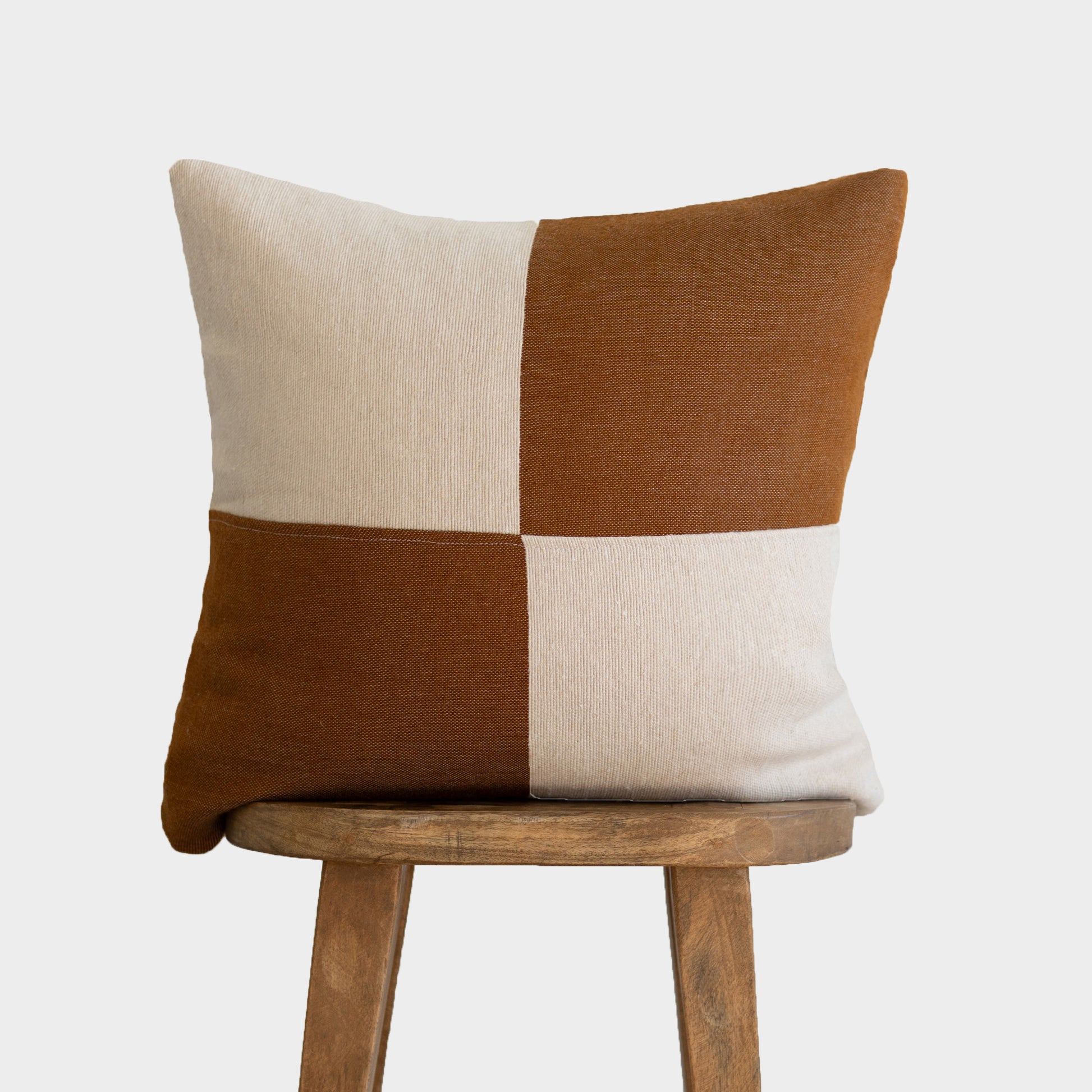 Brown and cream checkered pillow cover displayed on wooden chair back.