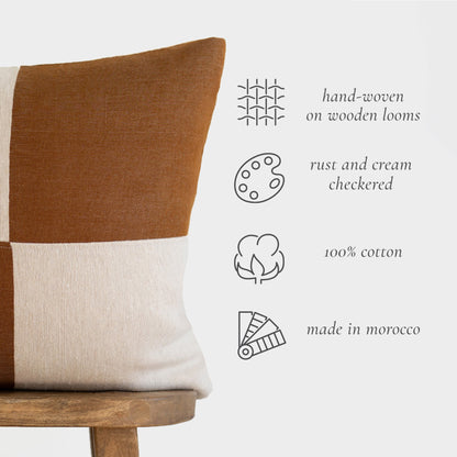 Rust and cream checkered 22-inch pillow with 100% cotton construction and color-blocked design on wooden chair.