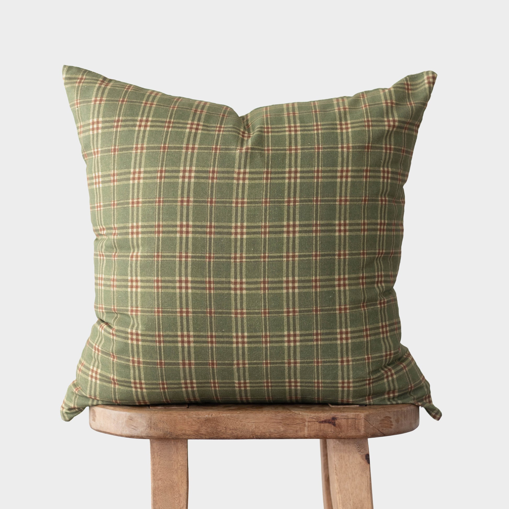 Green plaid throw pillow with cream and red stripes on wooden chair.