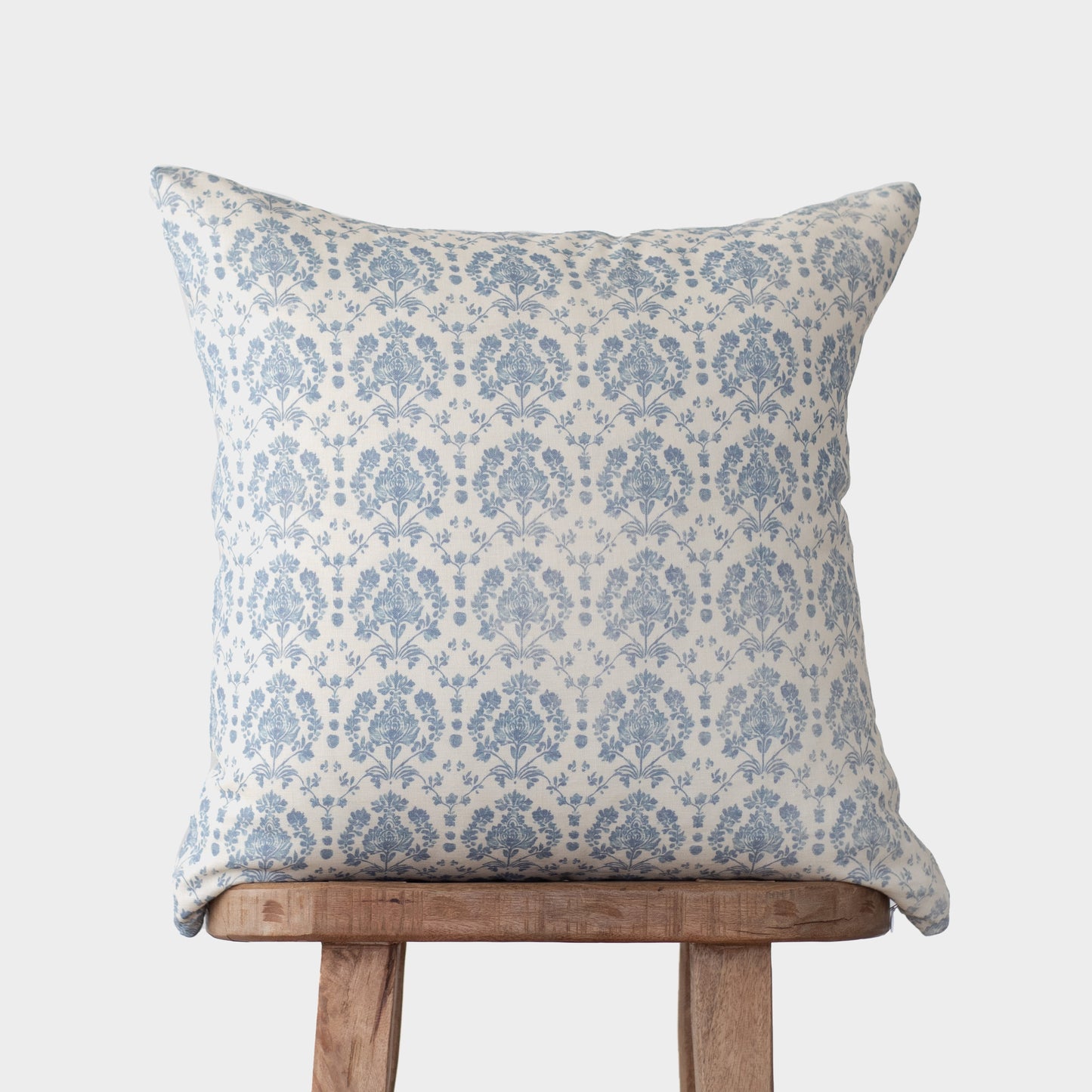 Blue and cream damask patterned linen pillow displayed on wooden chair back against gray background.