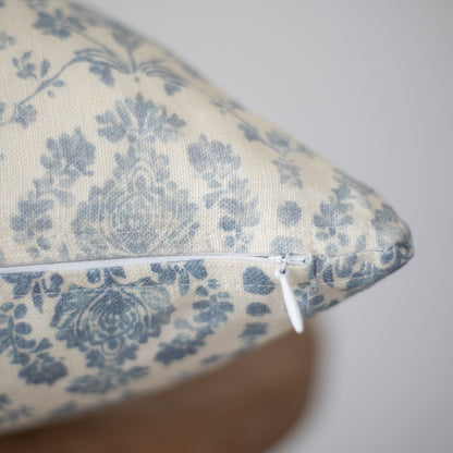 Cream linen pillow with blue floral damask pattern and white zipper closure.