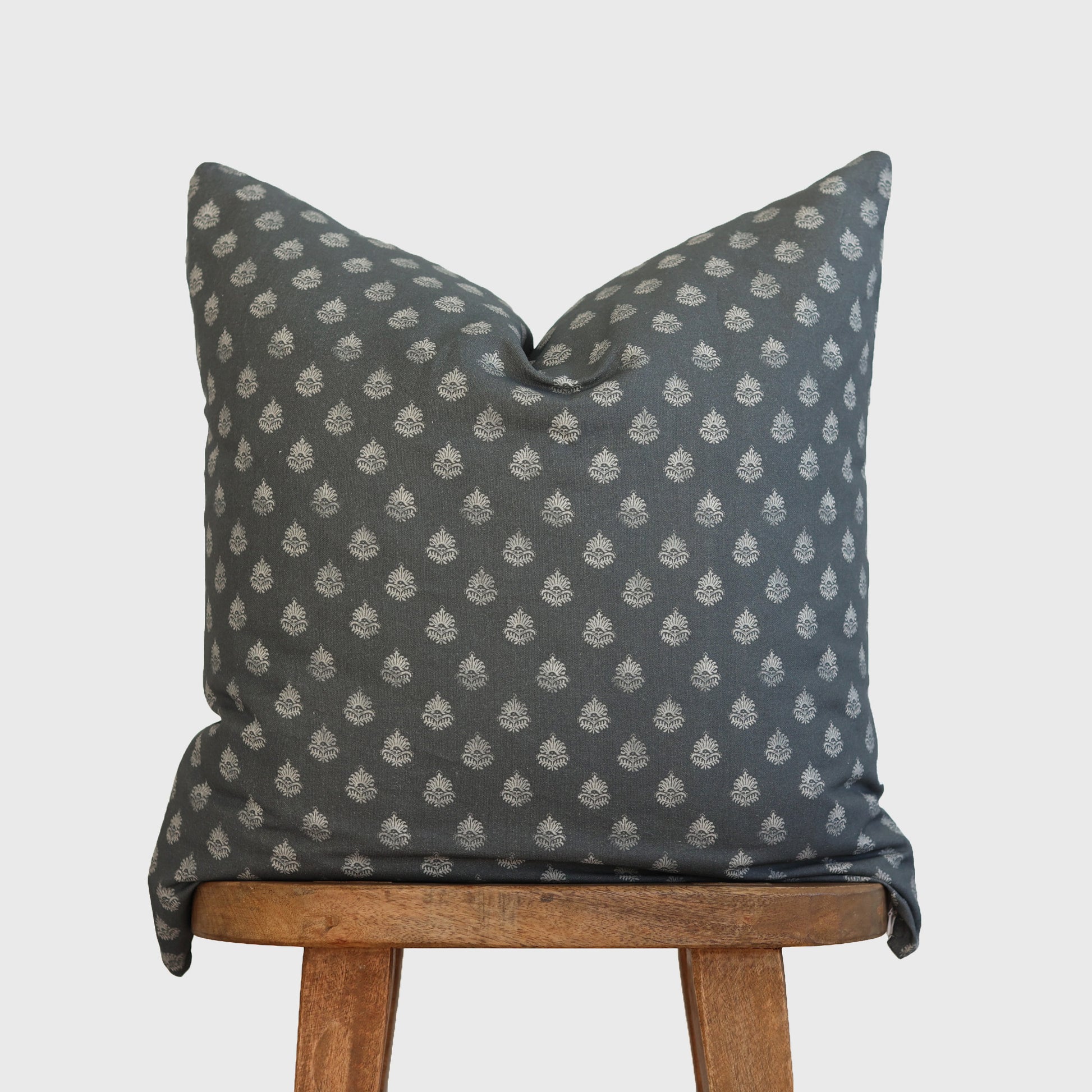 Blue-gray pillow with cream floral pattern displayed on wooden chair.