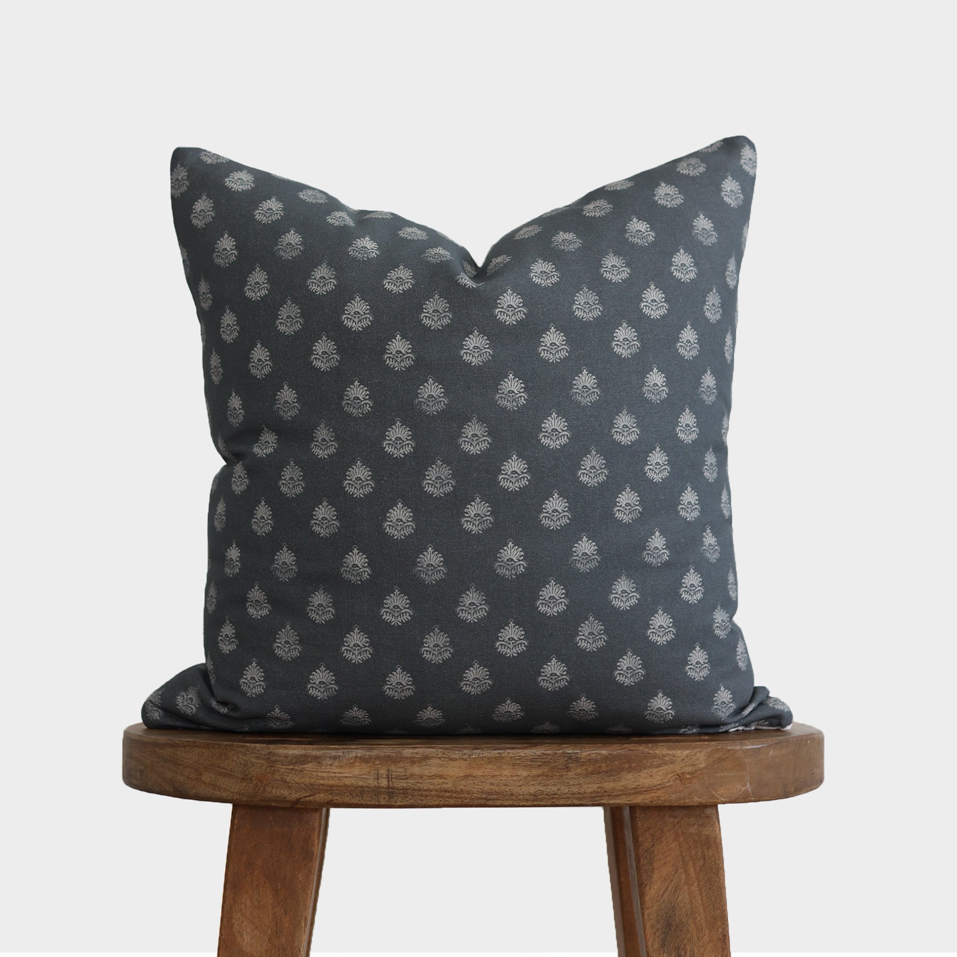 Dark blue pillow with repeating white geometric floral pattern, displayed on wooden stool.