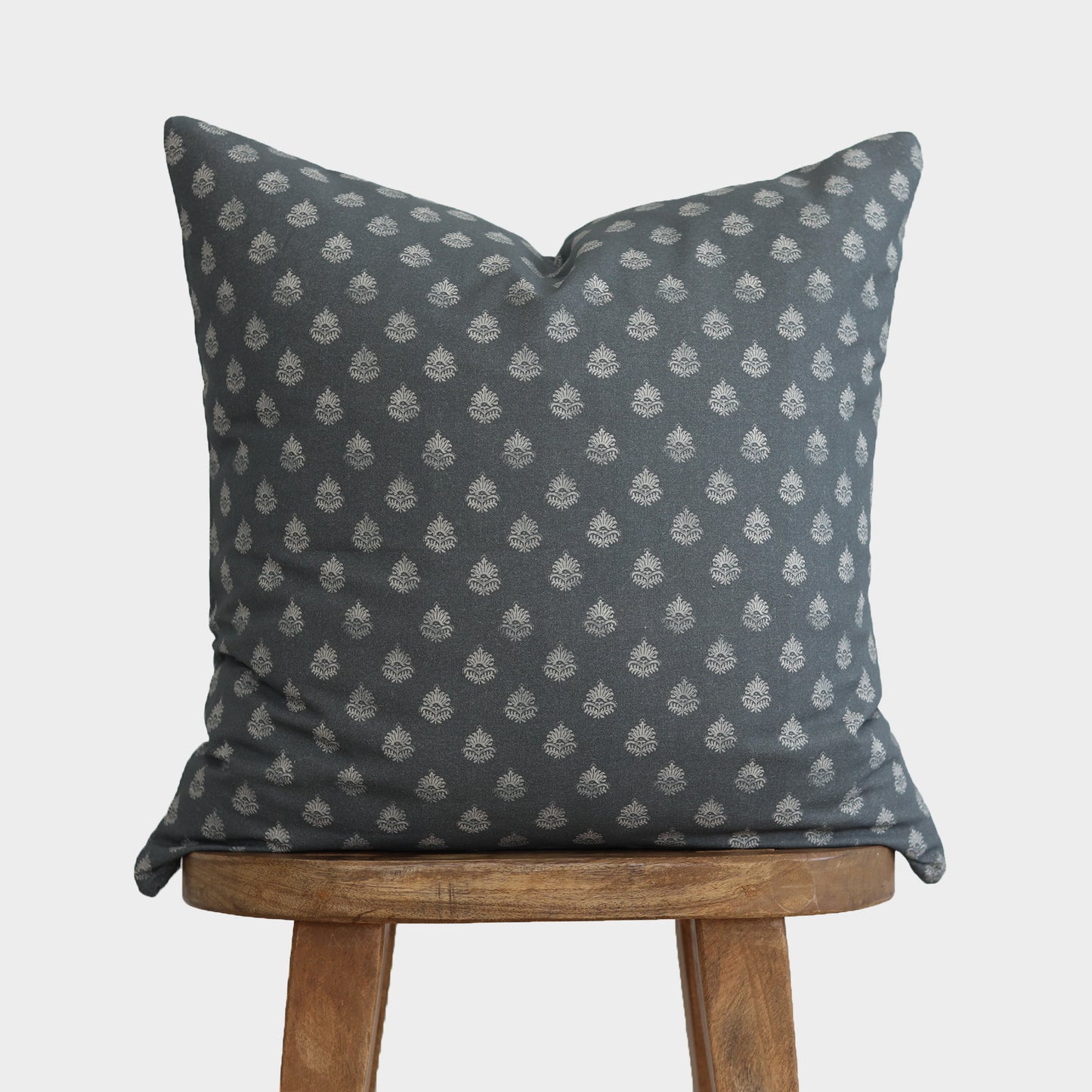 Blue-gray cushion with repeating white geometric floral pattern, displayed on wooden stool.
