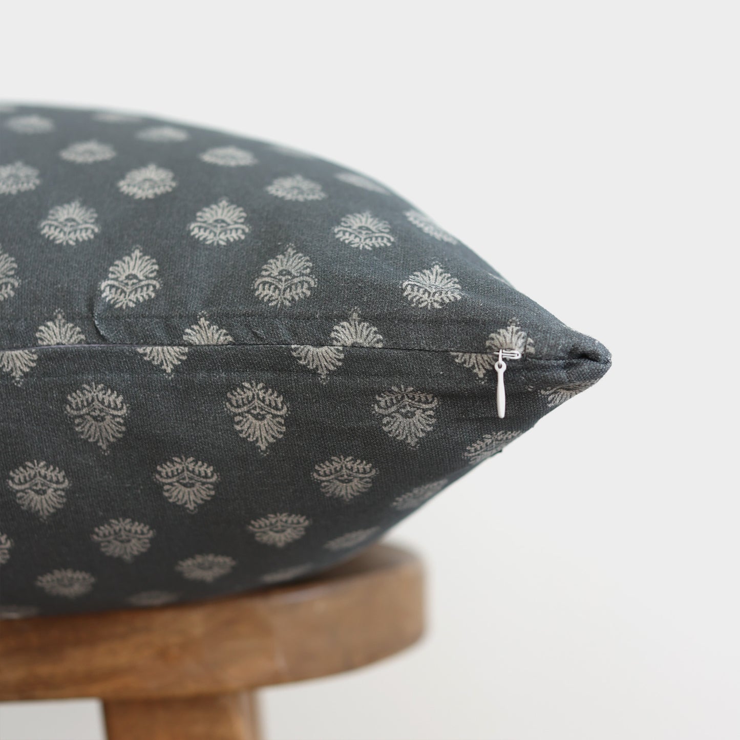 Blue-gray pillow with cream damask pattern and zipper detail resting on wooden stool.