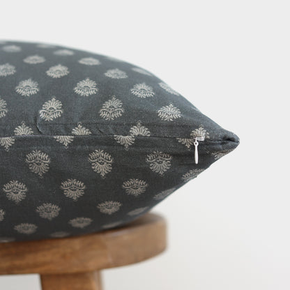 Blue-gray pillow with cream damask pattern and zipper detail resting on wooden stool.