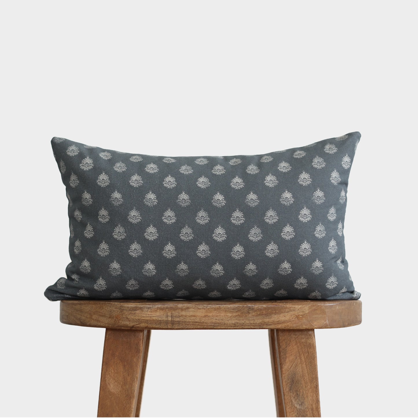 Blue-gray lumbar pillow with repeating cream circular flower motifs displayed on wooden stool.