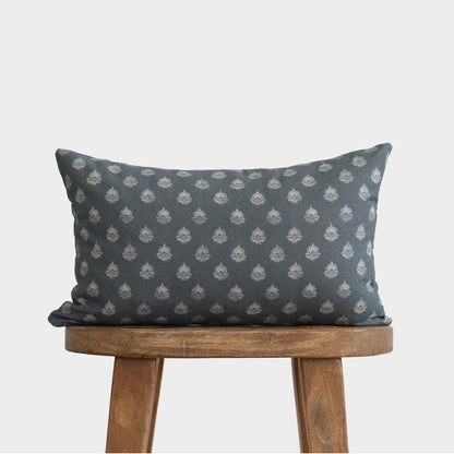Blue-gray lumbar pillow with repeating cream circular flower motifs displayed on wooden stool.