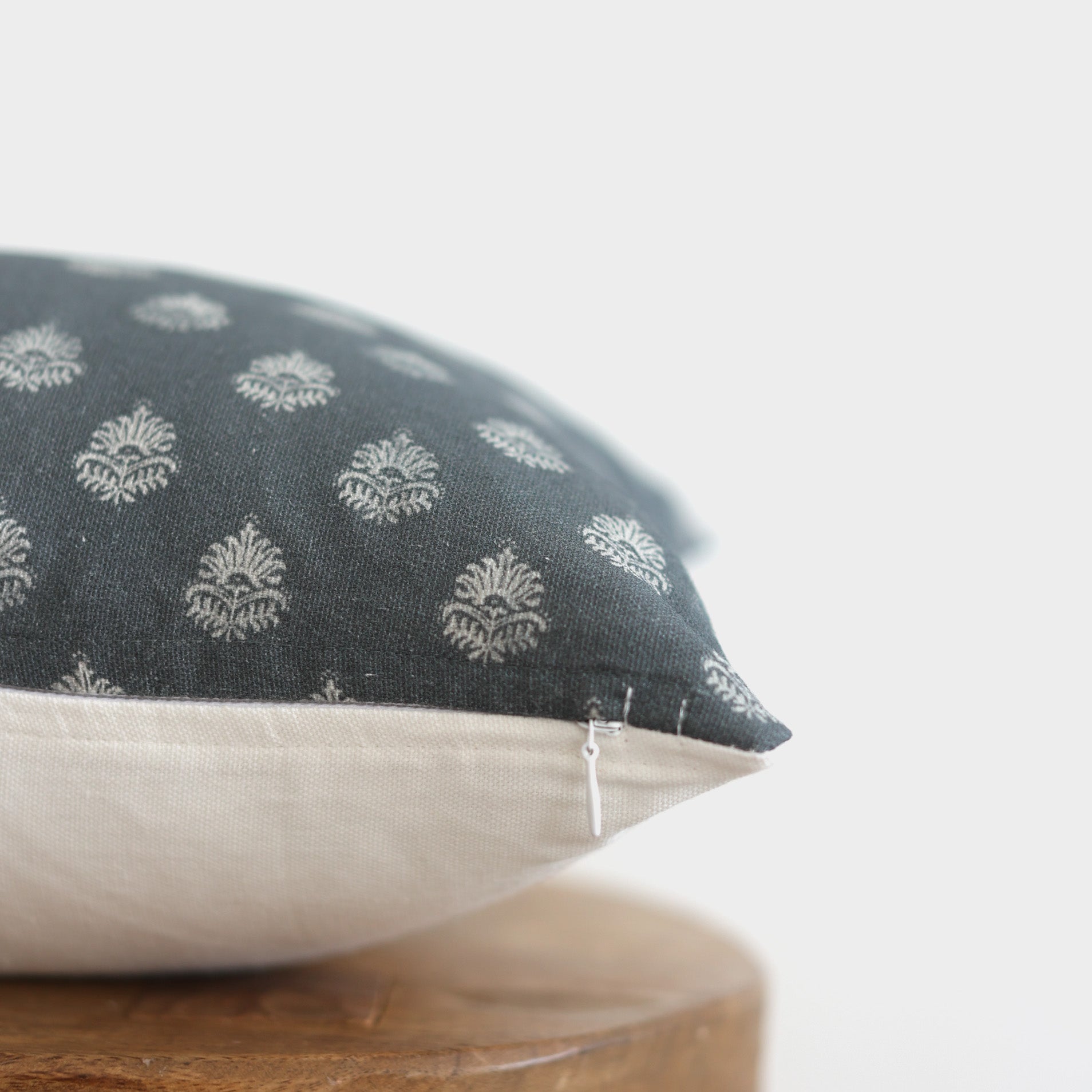 Decorative pillow with dark blue patterned top half featuring white damask motifs and cream linen bottom half on wooden surfa