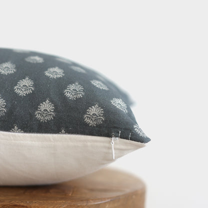Decorative pillow with dark blue patterned top half featuring white damask motifs and cream linen bottom half on wooden surfa