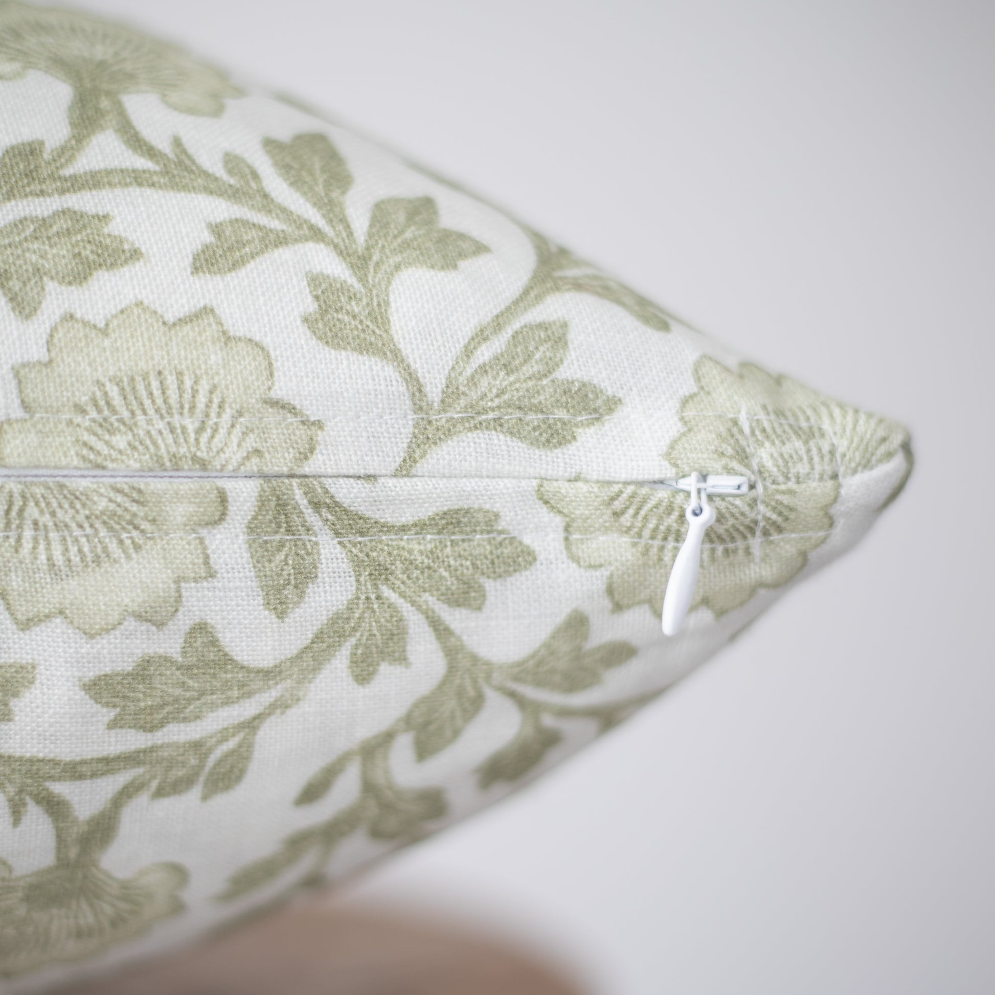 Sage green botanical print linen pillow with white zipper closure.