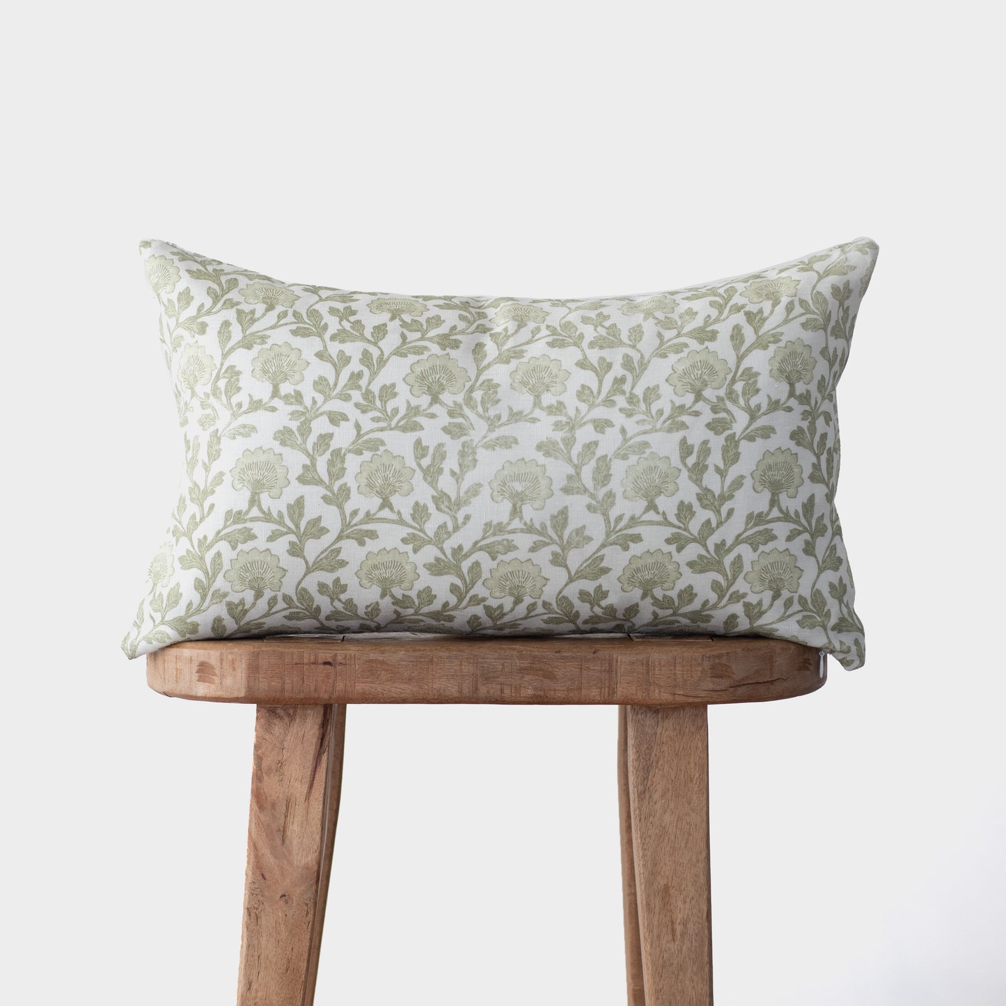 Rectangular linen pillow with sage green floral botanical print, displayed on wooden stool.