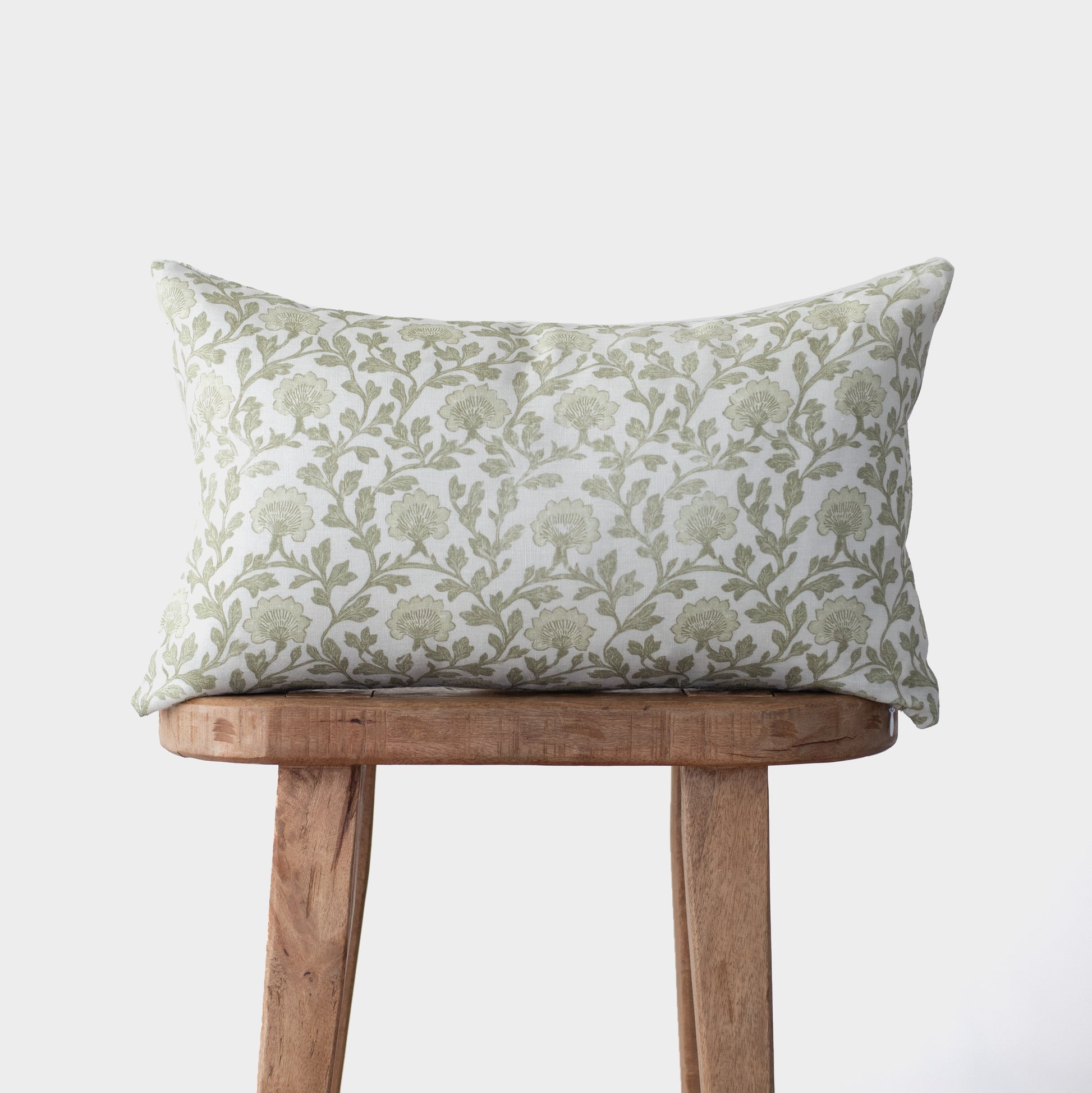 Rectangular linen pillow with sage green floral botanical print, displayed on wooden stool.