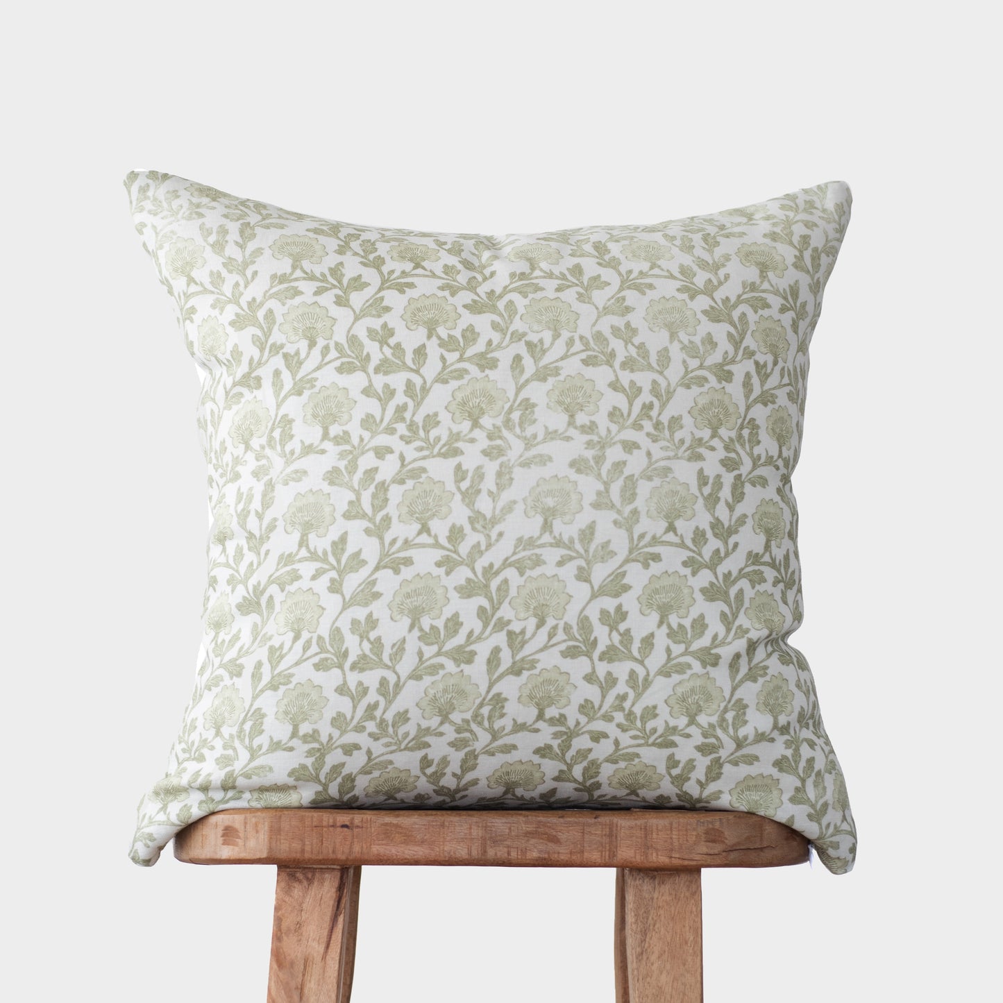 Cream linen pillow with sage green floral and leaf pattern, displayed on wooden chair.
