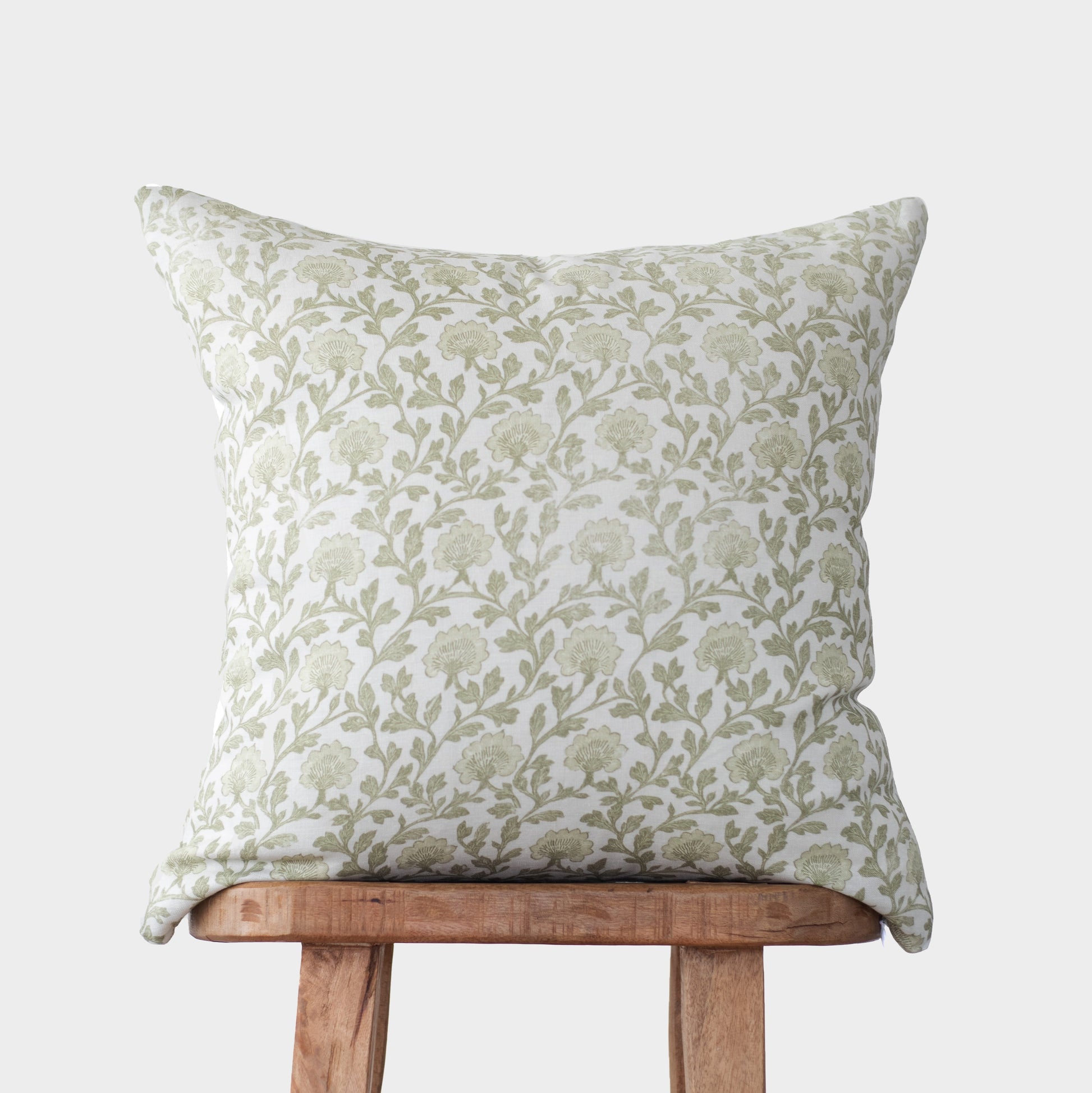 Cream linen pillow with sage green floral and leaf pattern, displayed on wooden chair.