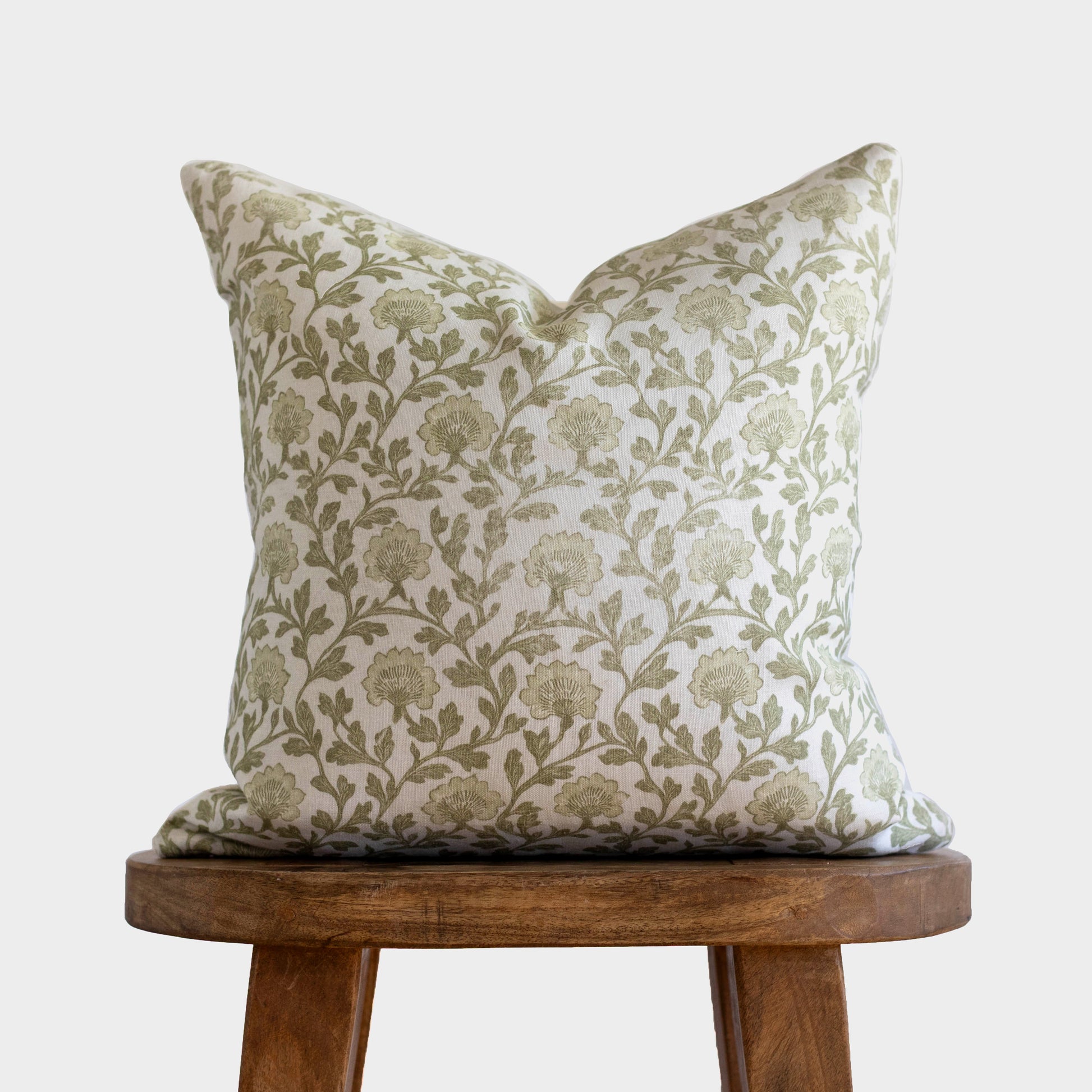 Cream linen pillow with sage green floral and leaf pattern, displayed on wooden stool.