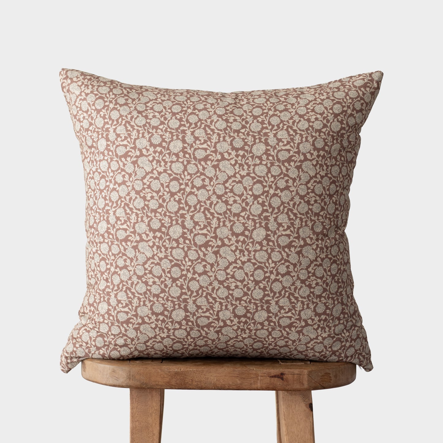 Tan and cream damask patterned throw pillow displayed on a wooden stool.