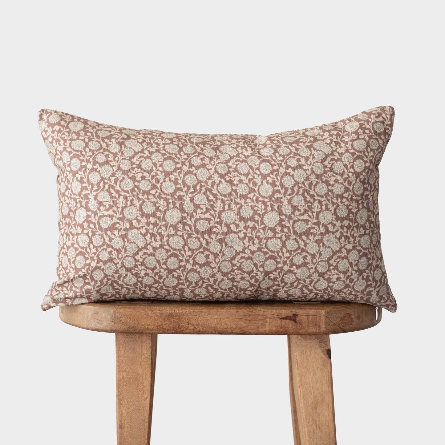 Rectangular throw pillow with rust and cream floral damask pattern resting on wooden chair.